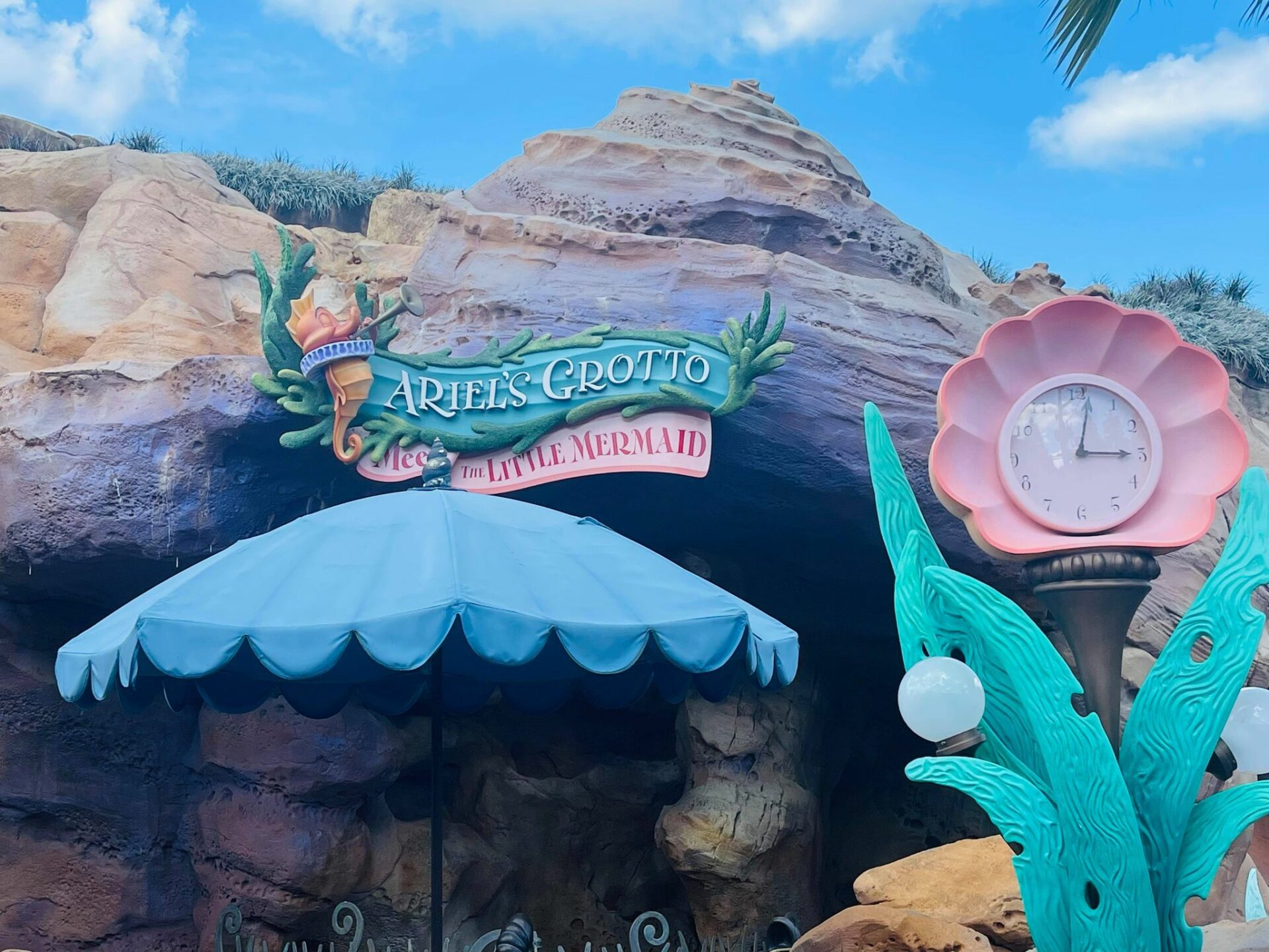Entrada da Ariel's Grotto na Fantasyland do Magic Kingdom, com a placa do encontro e o relogio em forma de concha