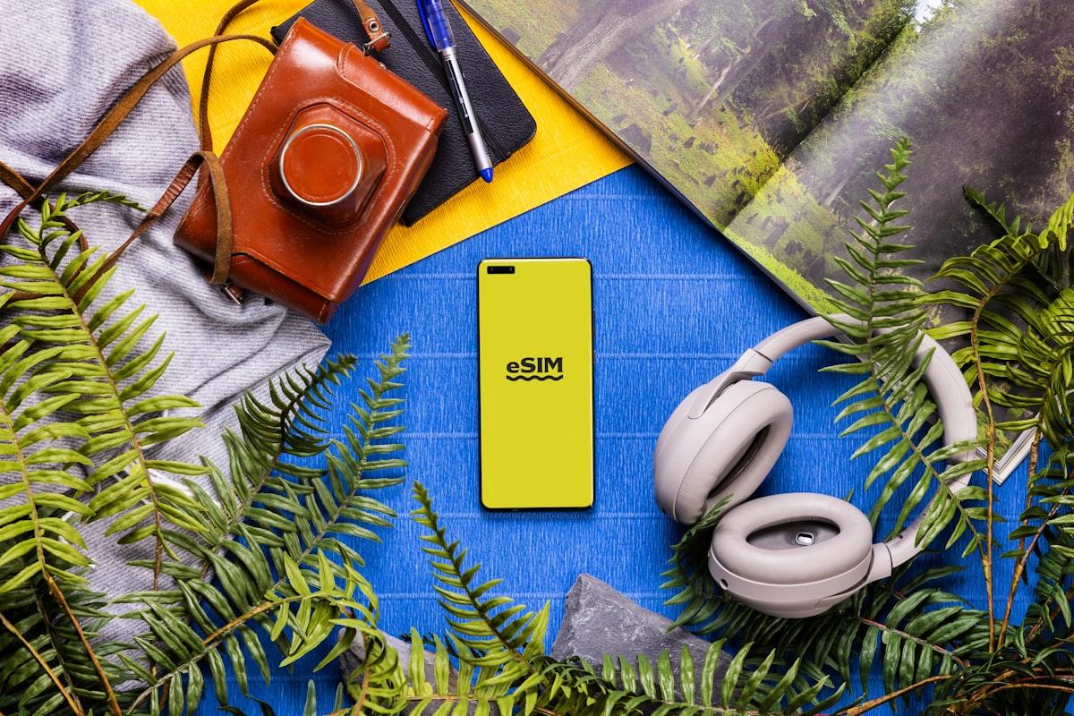 Itens de viagem dispostos sobre mesa — celular, câmera e fones de ouvido