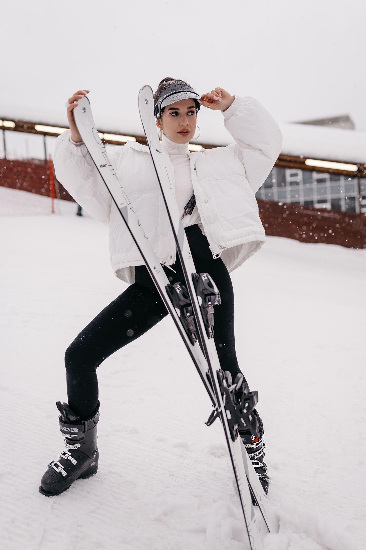 Esquiadora vestida com jaqueta térmica segurando os esquis na neve